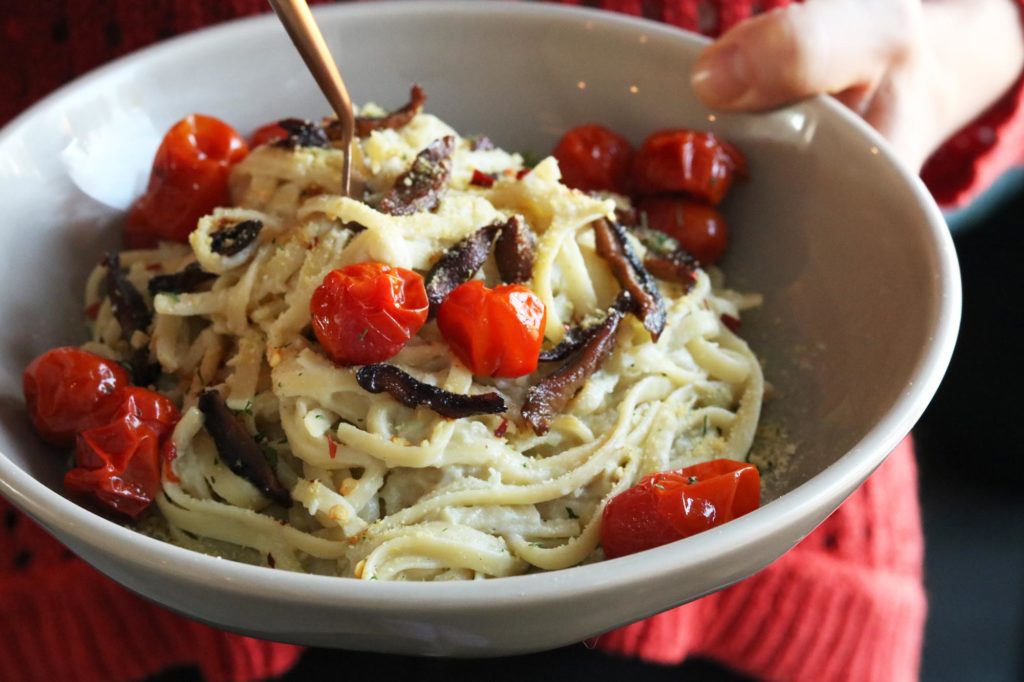 Bowl of artichoke carbonara pasta made with dairy-free cheese and topped with roasted tomatoes and shiitake bacon.