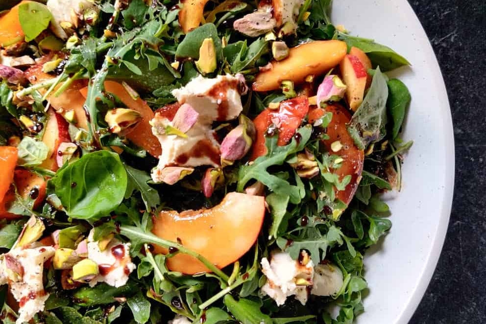 A salad of mixed greens, nectarines, chopped nuts, and dairy free brie cheese, drizzled with a balsamic dressing.