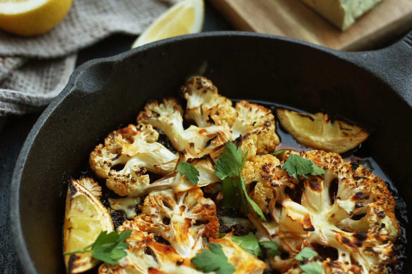 Frying pan with cooked buffalo cauliflower steaks drizzled in dairy free blue cheese sauce and lemon juice.