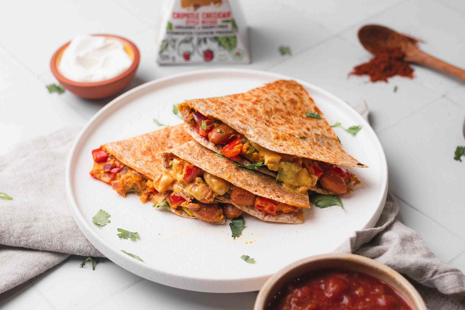 Prepared vegan cheesy bean quesadilla using chipotle cheddar dairy free cheese beside side dishes of salsa and dairy free sour cream.