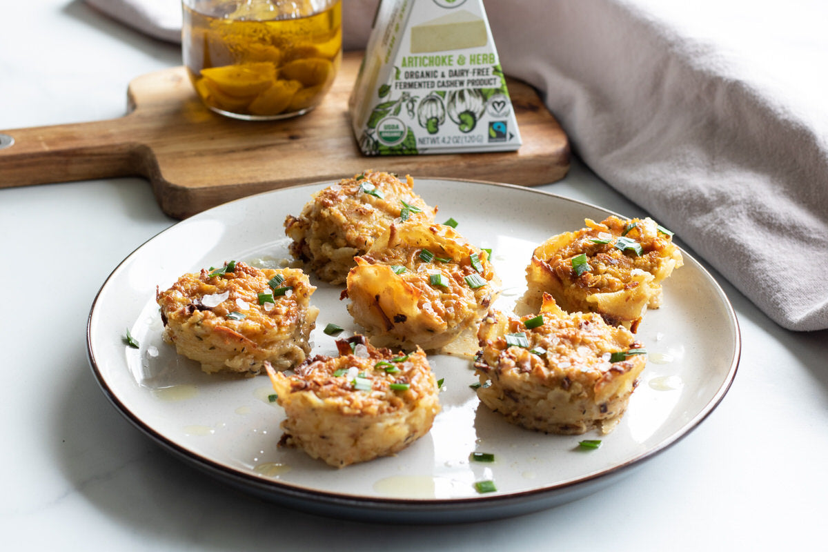 Plate of round stacks of cheesy vegan scalloped potatoes served next to a cutting board with dairy-free artichoke & herb cheese.