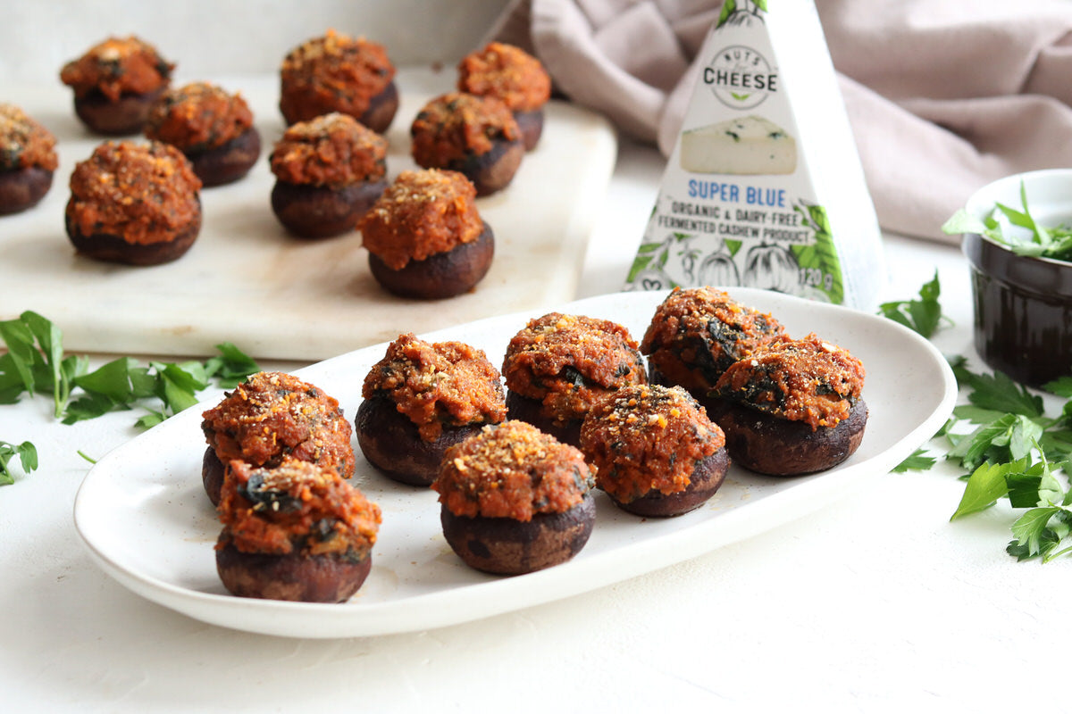 Two plates of baked mushroom caps stuffed with vegan chorizo sausage and dairy free blue cheese. Served next to a box of dairy-free blue cheese.