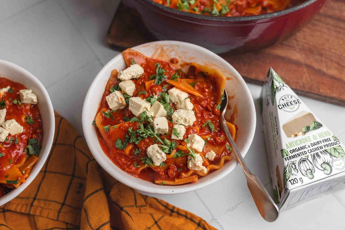 A bowl of vegan lasagna soup topped with pieces of dairy free artichoke and herb cheese.