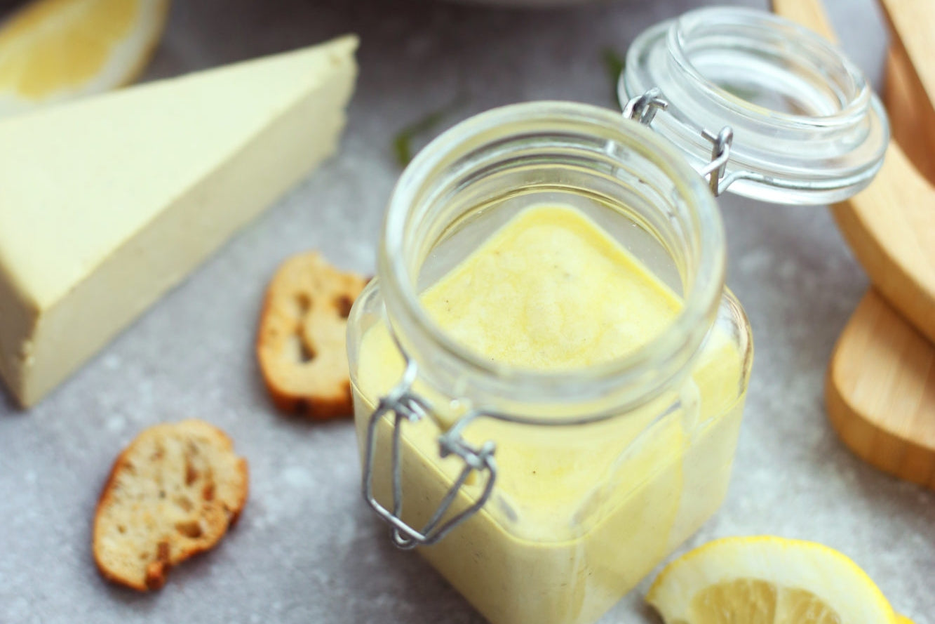 Jar filled with dairy-free caesar dressing served beside toasted croutons and a wedge of dairy-free brie cheese.