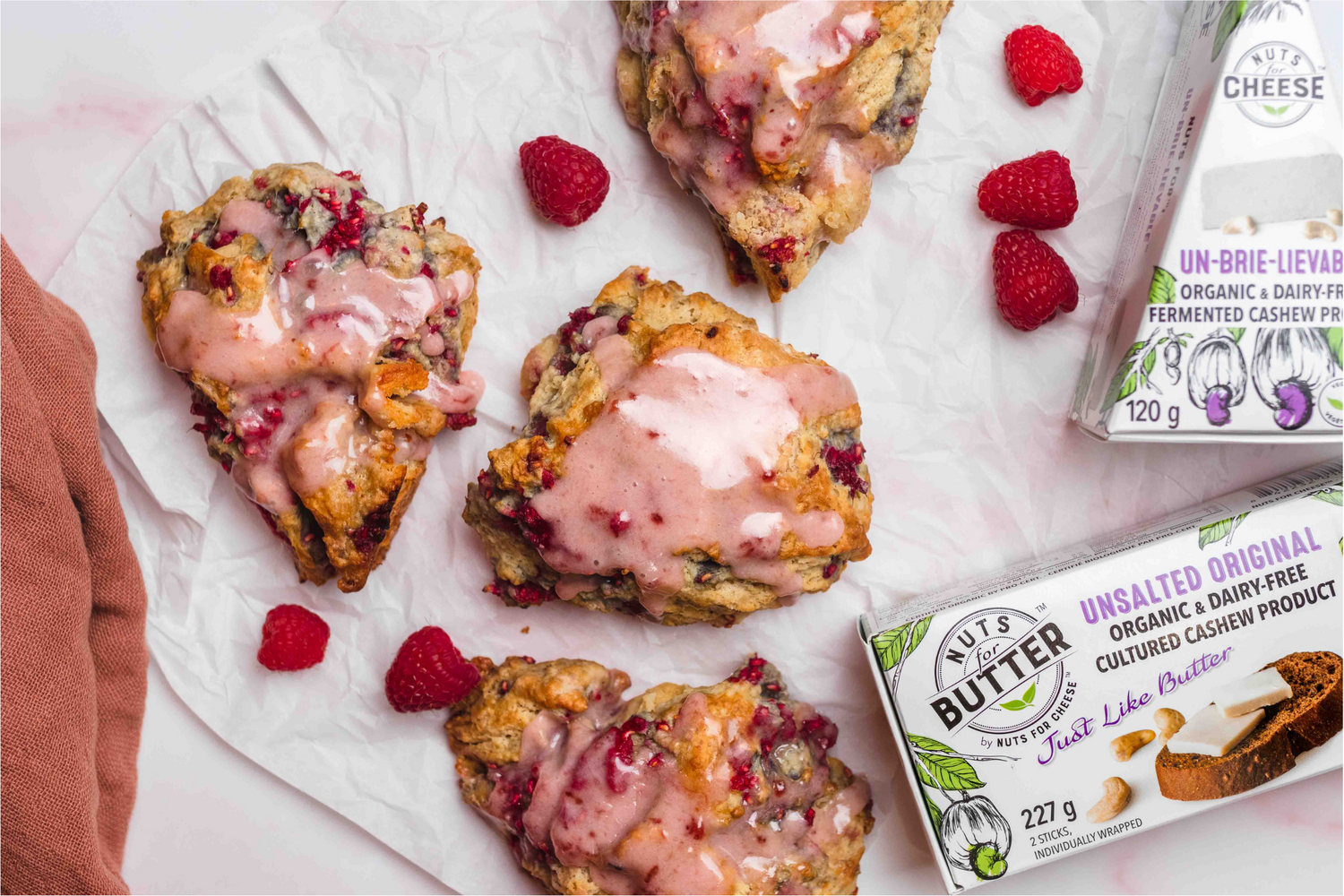 Vegan Raspberry Brie Scones with a Raspberry Glaze on a counter with a wedge of Un-Brie-Lievable and a box of Unsalted Original Butter
