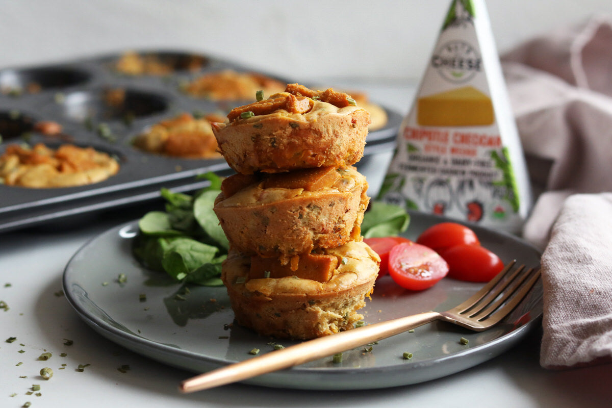 A stack of vegan frittata cups made with sweet potatoes and dairy-free chipotle cheddar cheese. served on a plate with a fresh green salad next to a box of dairy-free chipotle cheddar cheese.