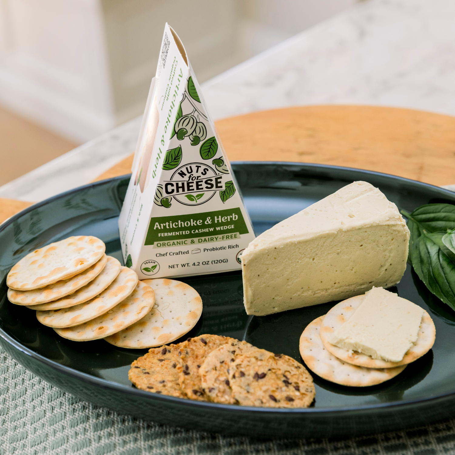 Nuts For Cheeses Artichoke & Herb wedge sur une assiette avec des crackers et du basilic.