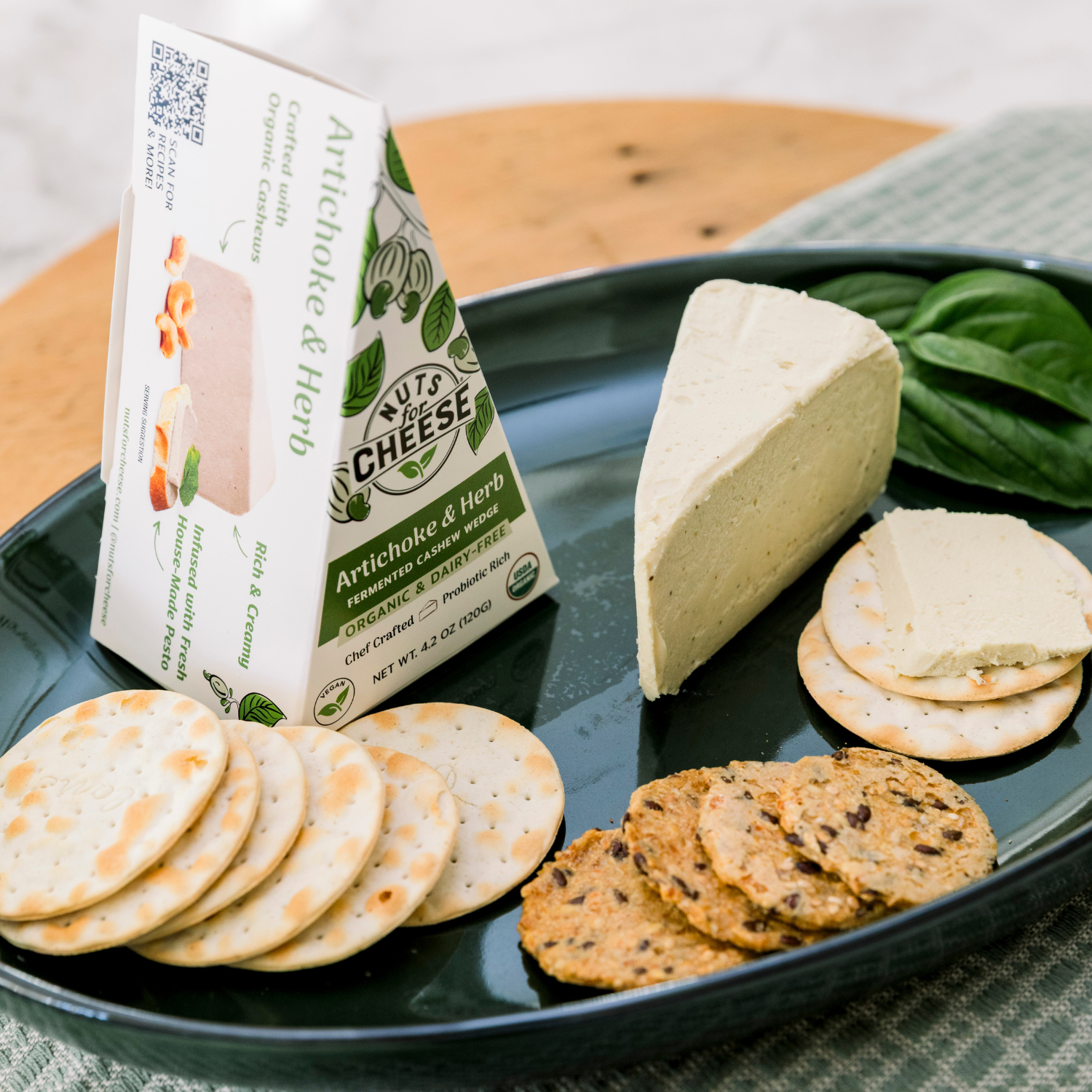 Plateau avec du fromage aux artichauts et aux herbes, des crackers et une boîte de fromage de cajou Nuts For Cheese Artichoke & Herb.