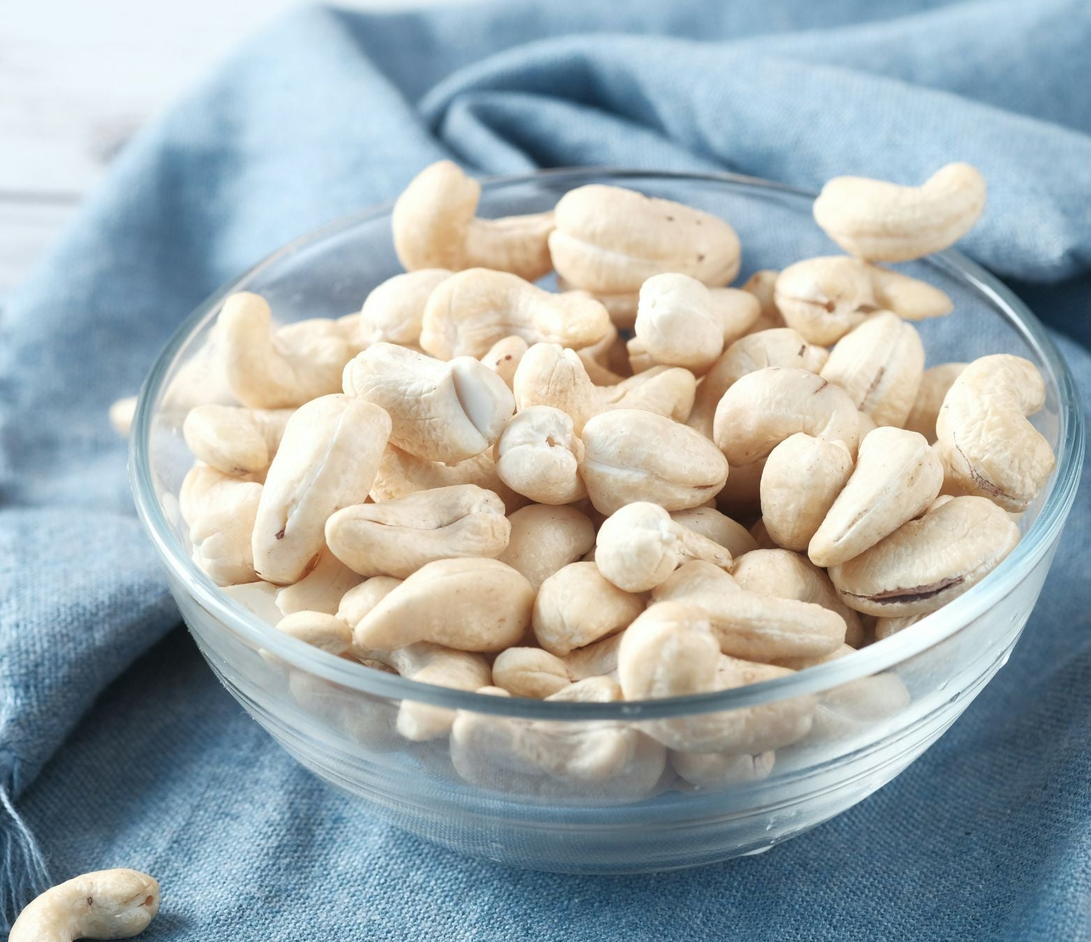 white cashews in a glass bowl on a blue tablecloth