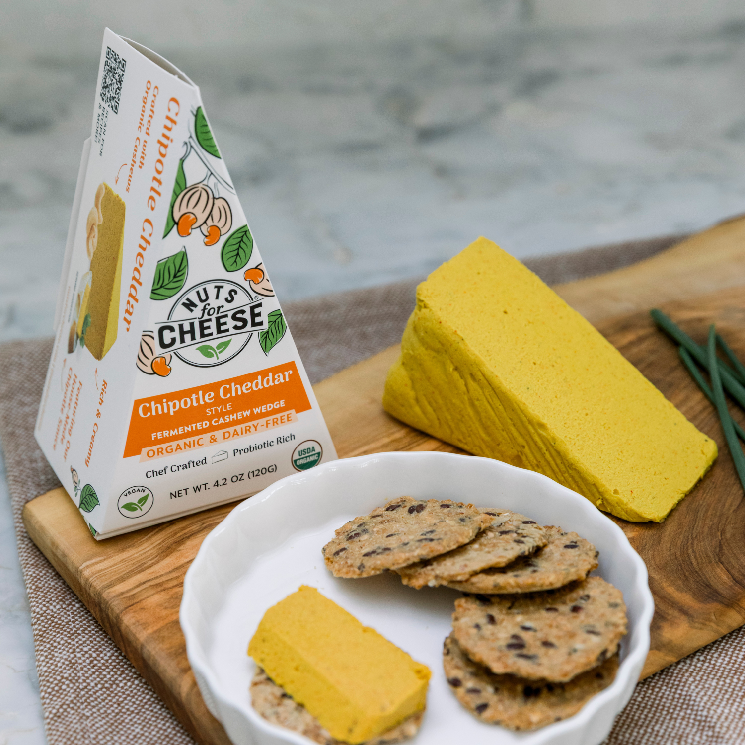 Tranche de Chipotle Cheddar de Nuts for Cheese sur une planche en bois avec des crackers.