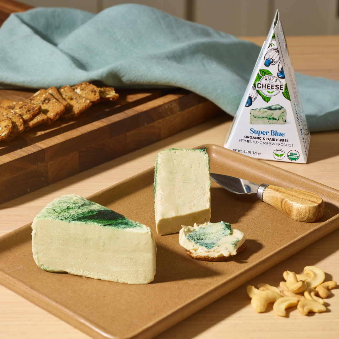 nuts for cheese dairy free super blue cheese wedge and package sitting on a brown serving board with cashews and crackers