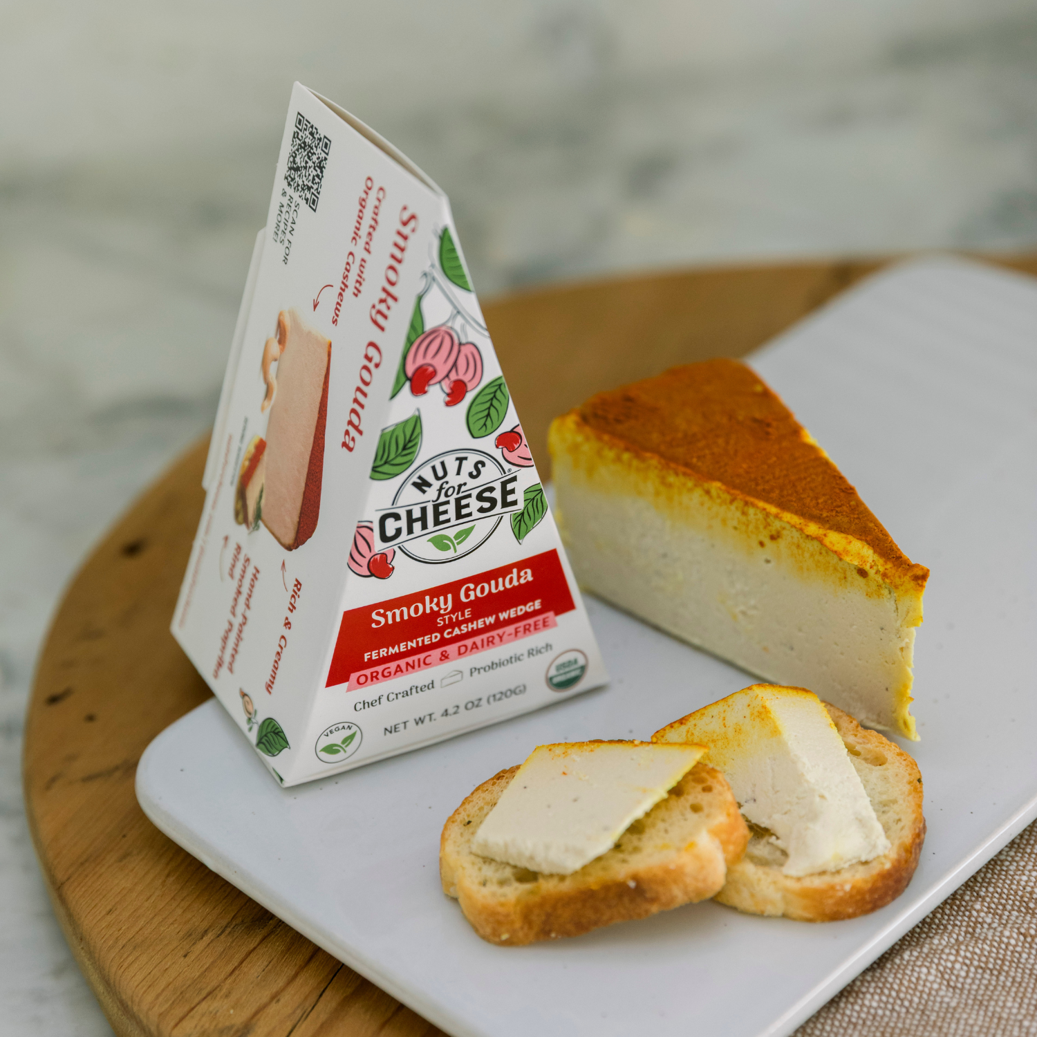 Boîte de Nuts for Cheese Fromage de noix de cajou au gouda fumé sur une assiette blanche avec des tranches de pain et de fromage.