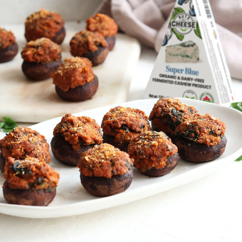 Plated plant-based sausage and cheese stuffed mushrooms with Nuts For Cheese™ Organic & dairy-free fermented Super Blue cheese wedge package