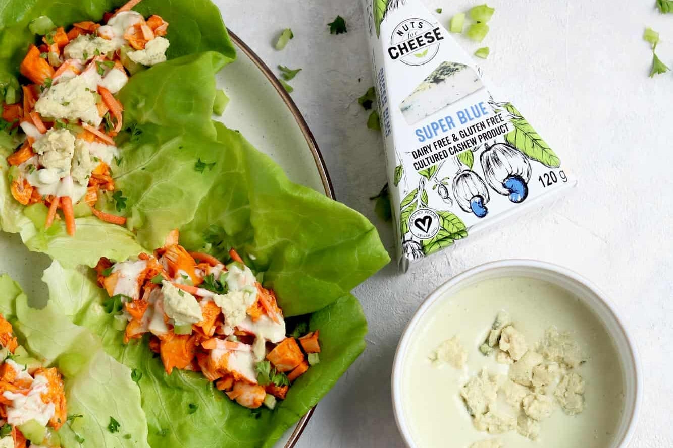 Lettuce wraps filled with buffalo-style pulled jackfruit and drizzled with dairy-free blue cheese sauce. Served with a bowl of dairy-free blue cheese sauce next to a box of dairy-free blue cheese.