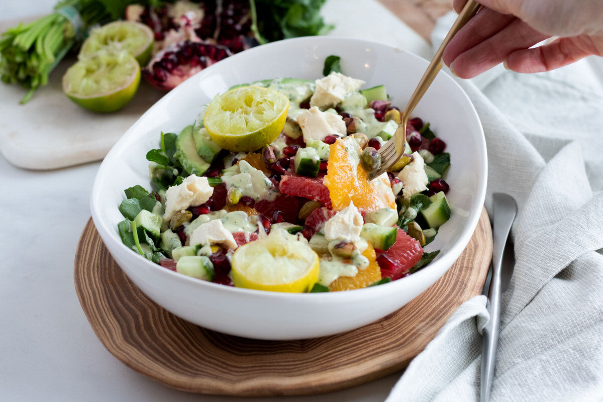 A bowl of colourful citrus salad featuring oranges, grapefruit, lemon, lime, and pomegranate, drizzled with a dairy-free cilantro crema dressing..