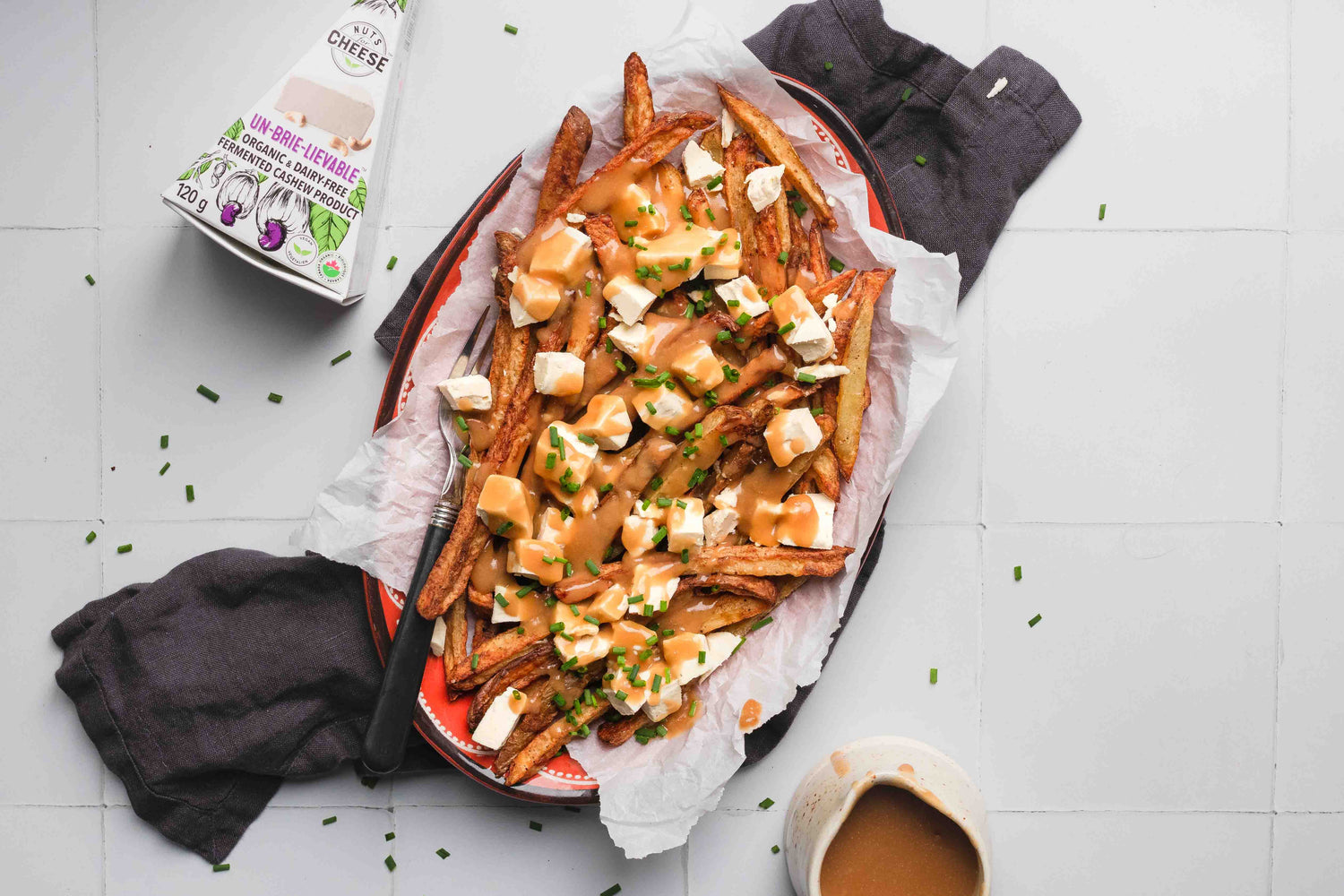 Prepared dish of vegan classic poutine using dairy free brie, set on a napkin with a side of plant based gravy.
