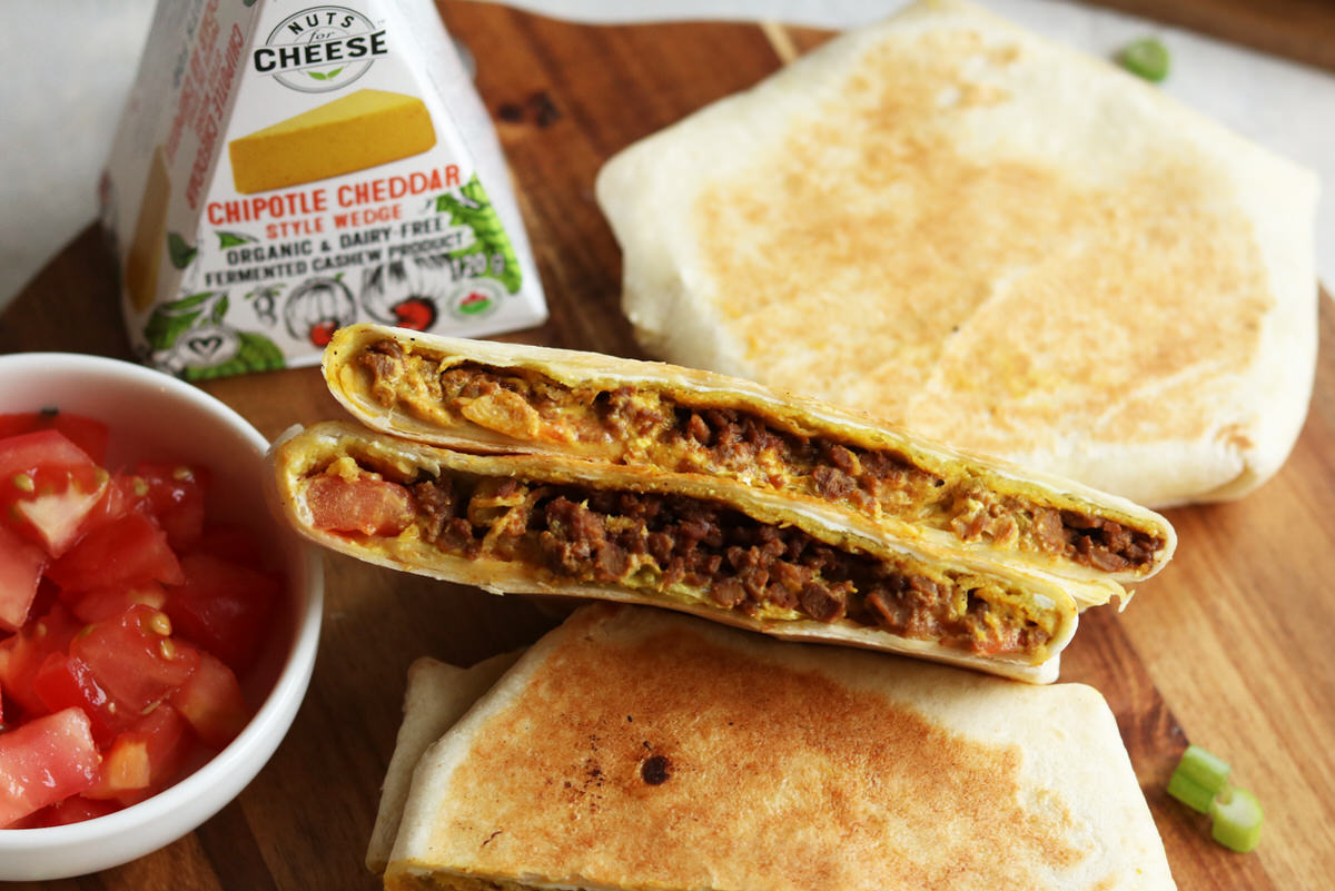 Toasted crunchwraps on a cutting board, stuffed with vegan cheese and veggie ground. Served with a side of fresh tomato salsa and beside a box of dairy-free chipotle cheddar cheese.