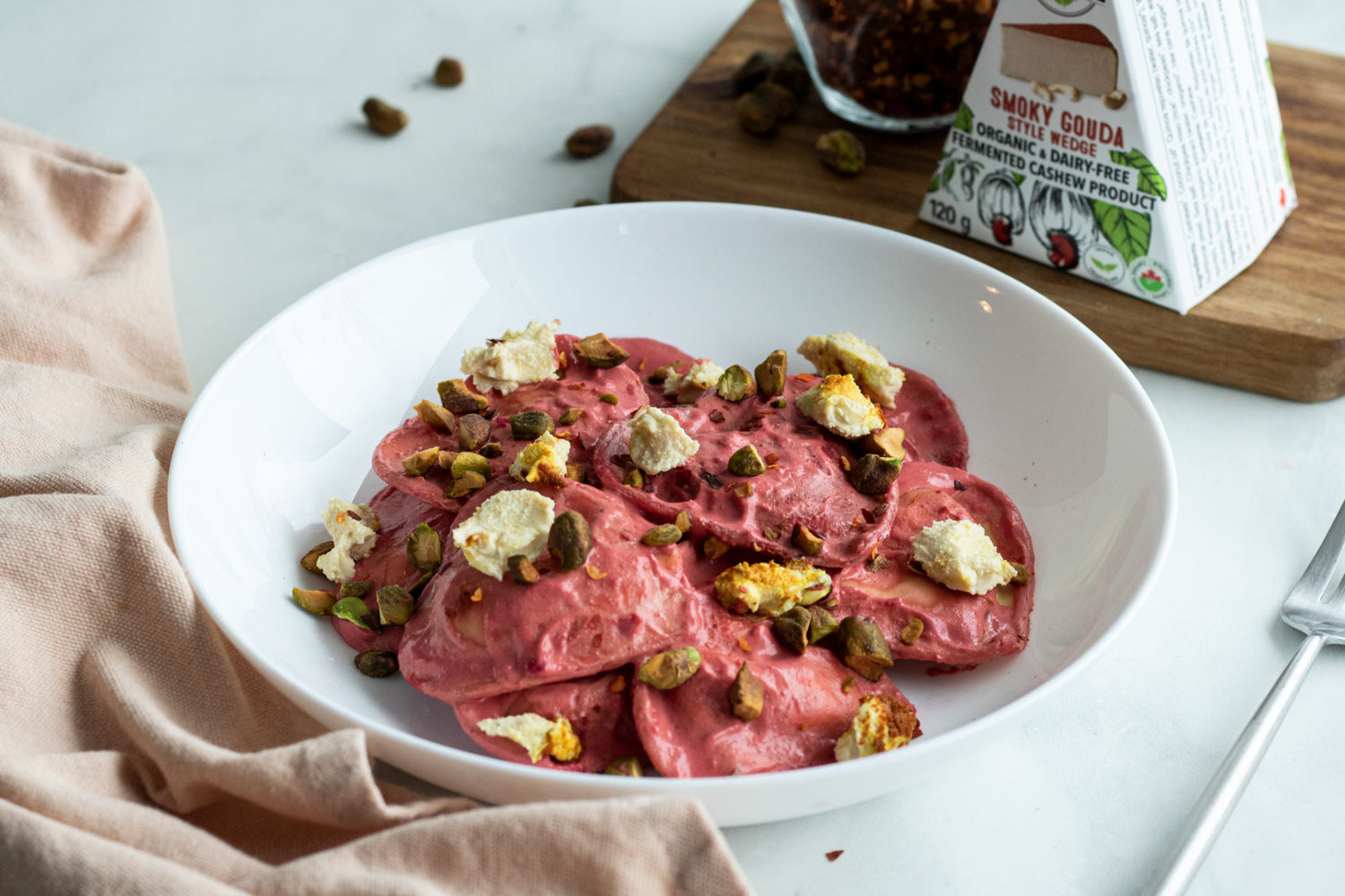 Bowl of pink, dairy-free beet ravioli topped with nuts and dairy-free smoked gouda cheese.