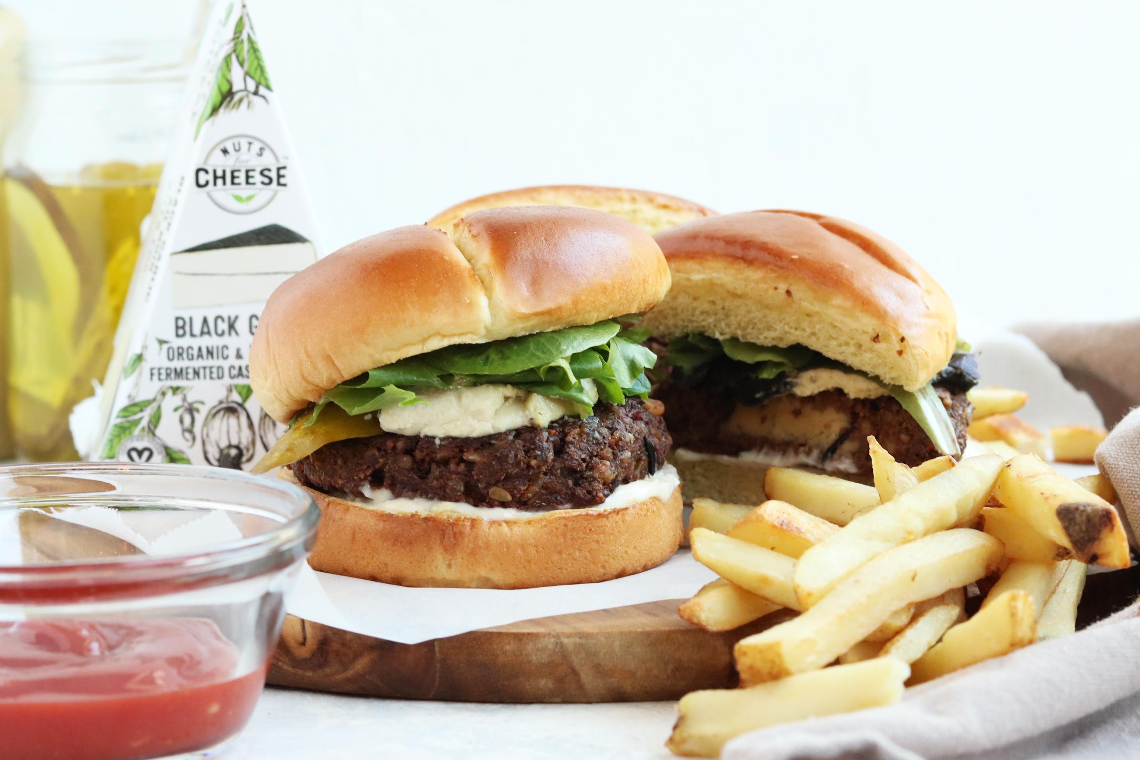 Prepared burgers on a plate, stuffed with dairy-free black garlic cheese and topped with lettuce. Served with fries and beside a box of dairy-free black garlic cheese.