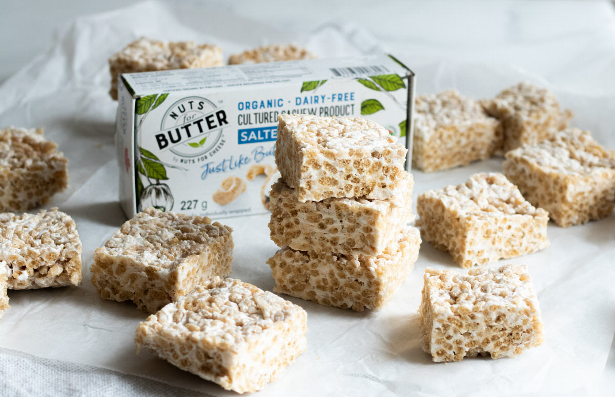 Rice crispy squares are scattered about and stacked in piles. Made with dairy-free butter, a box of dairy-free brown butter can be seen in the background.