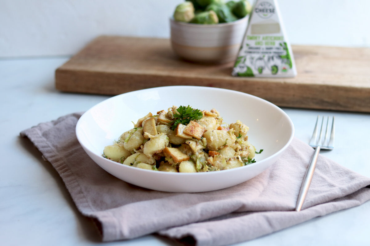 Bowl of cooked gnocci and shredded brussels sprouts topped with slices of smoked tofu. Served beside a wedge of dairy-free artichoke & herb cheese.