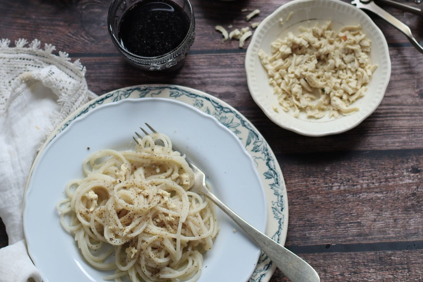 Bowl of vegan cacio e pepe noodles with dairy-free cauliflower sauce. Served next to a bowl of shredded dairy-free cheese.