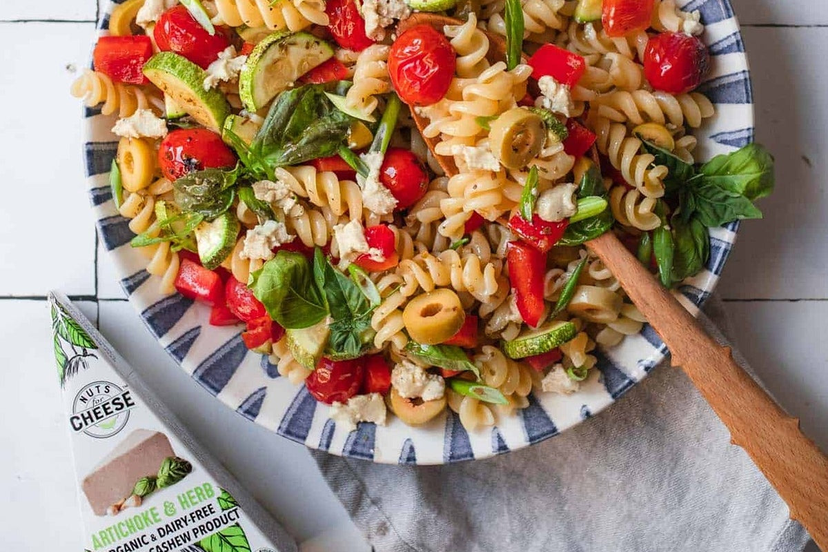 Large bowl of vegan pasta salad featuring grilled vegetables and pieces of dairy free artichoke & herb cheese.