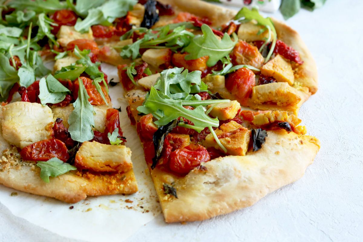 Prepared pizza made with dairy-free gouda cheese, sundried tomatoes, arugula, and cherry tomatoes.