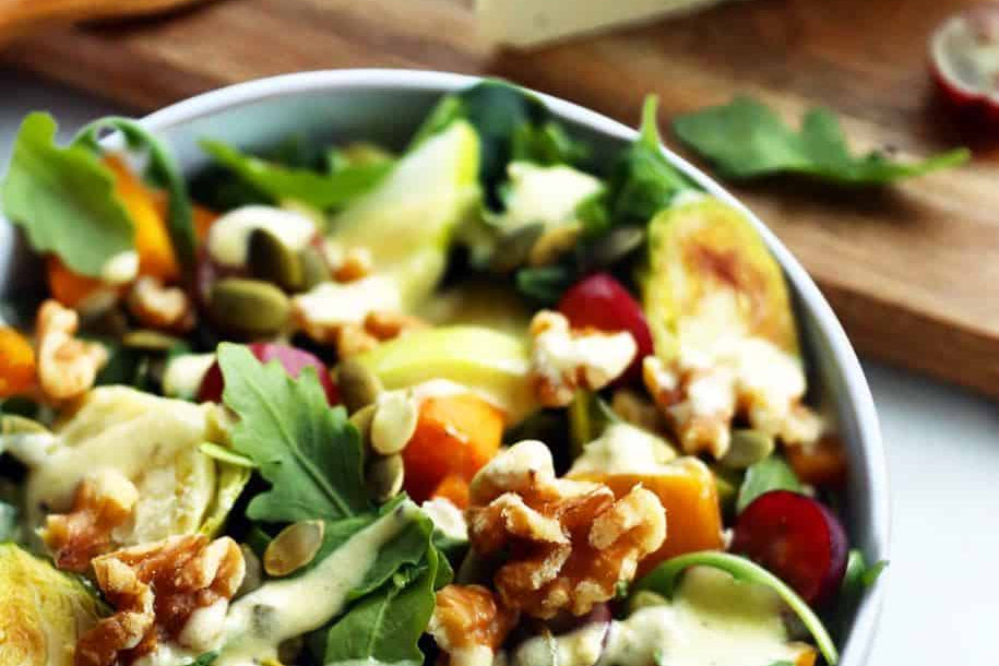 Bowl of Waldorf salad featuring fresh greens, roasted brussels sprouts, walnuts, grapes, and dairy-free blue cheese.
