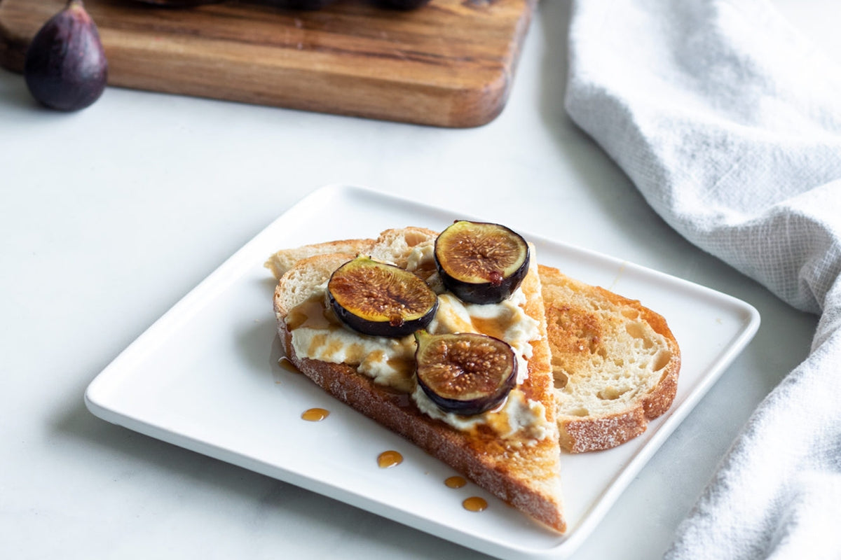 Sourdough toast on a plate, topped with vegan brie cheese and sliced fresh figs.