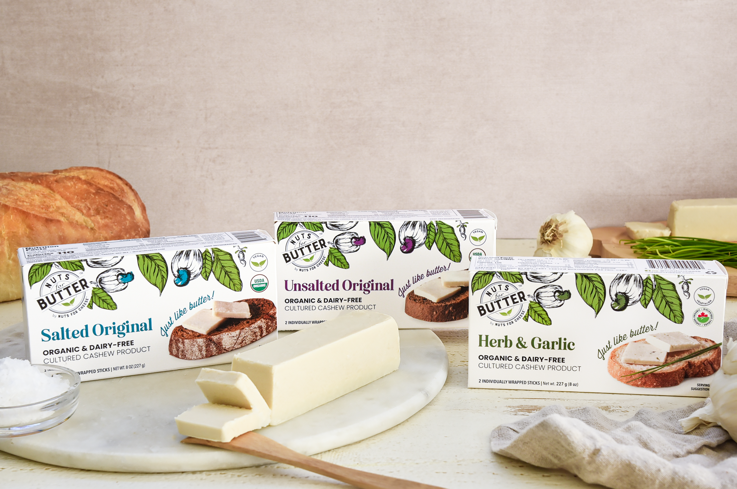 Nuts For Butter dairy-free butter packages next to a bar of plant-based butter sliced on a marble board.