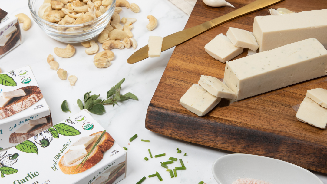 herb and garlic cashew based butter sitting on a table with a bowl of cashews, garlic and cashew butter wedges