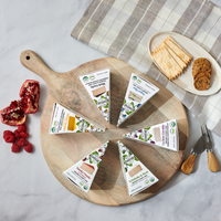 Nuts For Cheese wedges in packaging on a cheese board with fruit and crackers around it