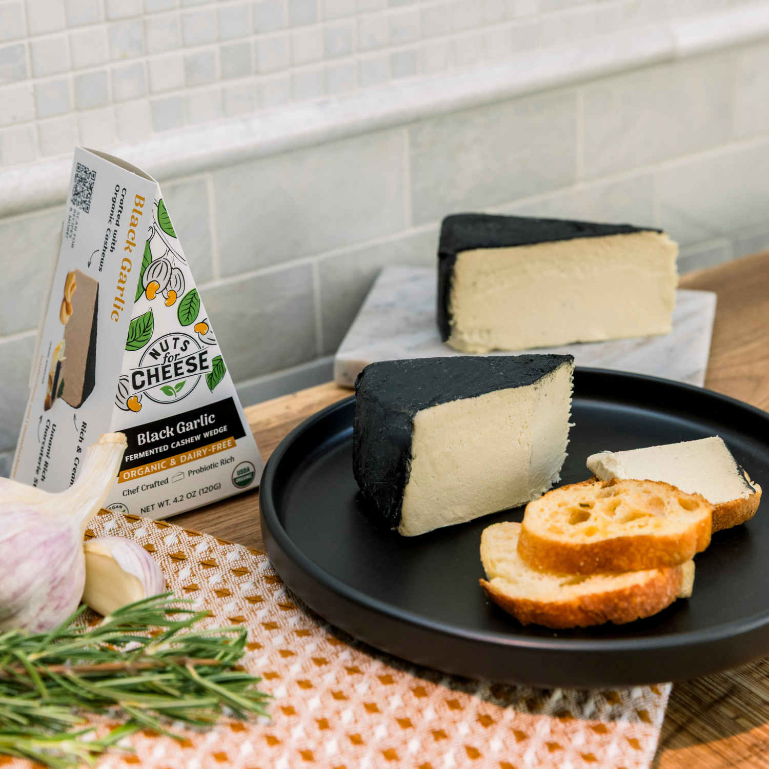 Nuts For Cheese Fromage de cajou à l'ail noir sur une assiette avec du pain et un emballage en arrière-plan.