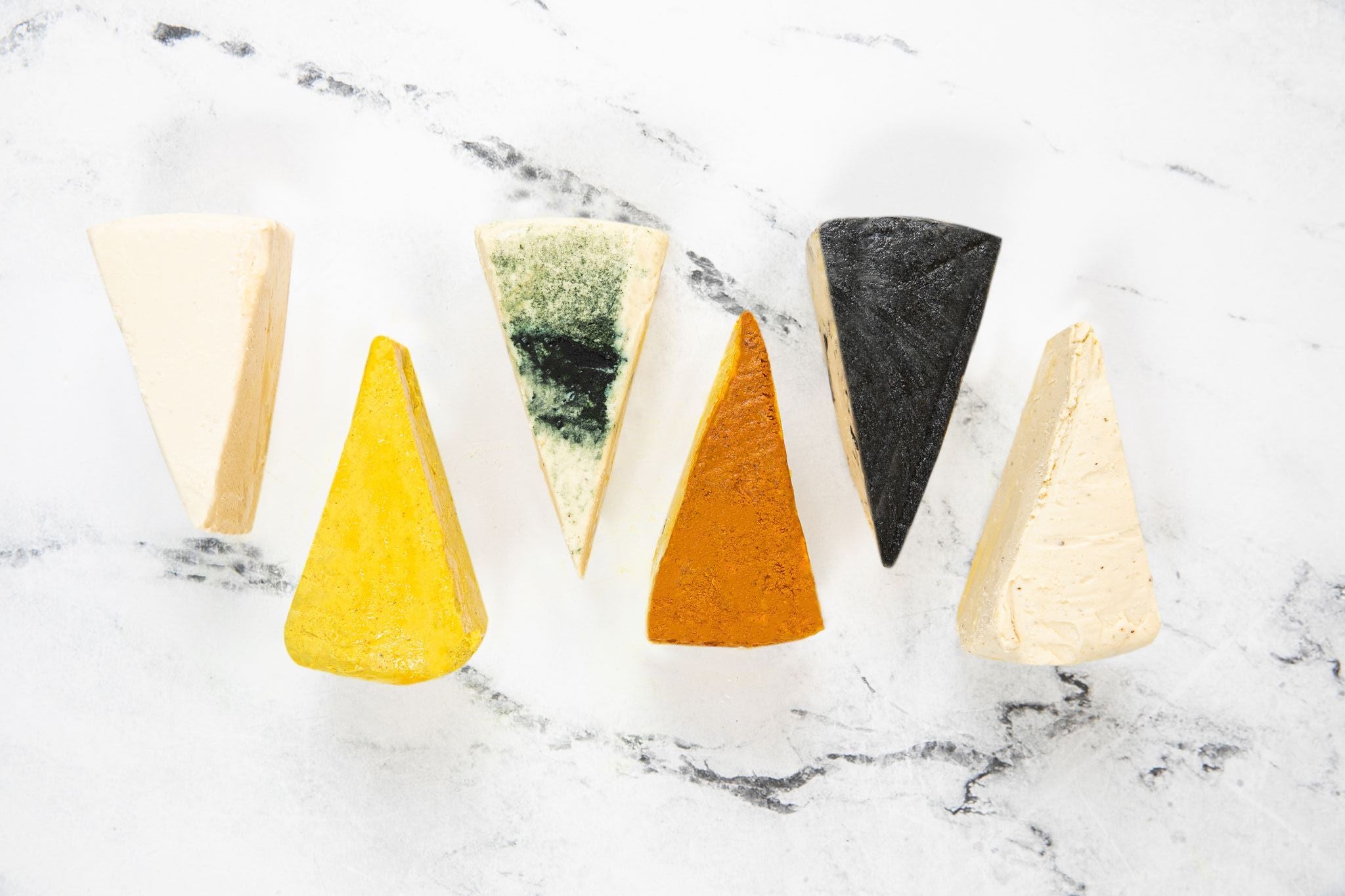 6 Flavours of Nuts For Cheese™ dairy-free cheese wedges on a white marble countertop