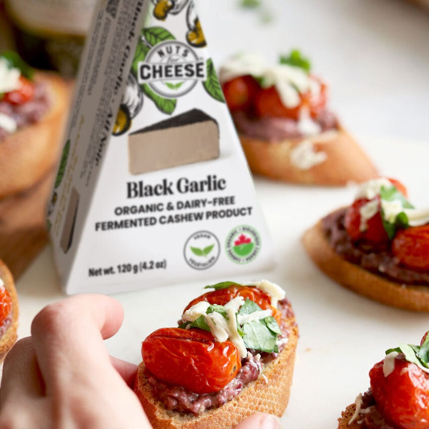Nuts For Cheese Black Garlic dairy-free cheese wedge next to slices of toast topped with bruschetta